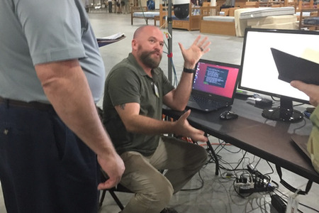 man sitting in front on a laptop with ubuntu on it gesturing his hands in a wide motion while talking
